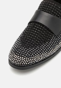 Black embellished shoe featuring a textured upper with black and silver studded rhinestones, smooth black leather strap across the midfoot.