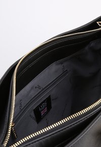 Svart läderväska med ett fack med dragkedja och en slät tygfoder inuti. Guldzipperdetaljer ger kontrast till designen.