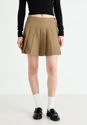 Khaki pleated mini skirt with a fitted waistband, featuring sharp creases, and a smooth texture. Paired with black loafers and white socks.
