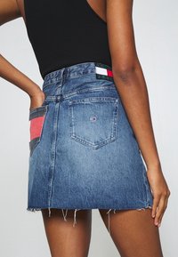 Denimkjol i medelblått med fransad fåll. Har en röd och marinblå läpp på bakfickan och en märkesetikett i midjan.