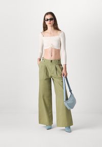 Vit ribbad crop top med knytning fram, olivgröna vida byxor, ljusblå handväska och matchande klackstövletter. Släta texturer.