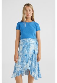 Blauwe t-shirt gecombineerd met een knie-lange, asymmetrische rok in een blauw en wit abstract patroon, met een gerimpelde zoom en een zijstrikje.