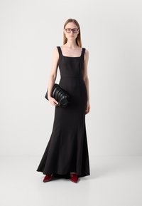 Black fitted dress with square neckline, flared hem, paired with a black pleated clutch and red pointed toe heels. Smooth texture.