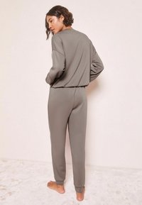 Šedý sportovní komplet, který zahrnuje volně střiženou mikinu s dlouhými rukávy a kalhoty s elastickým pasem, a vykazuje hladkou texturu a zúžené manžety.