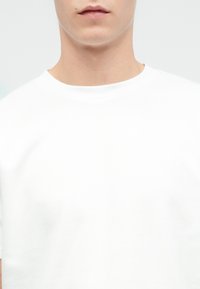 Λευκό βαμβακερό μπλουζάκι με στρογγυλή λαιμόκοψη, κοντά μανίκια και λεία υφή. Χωρίς ορατά σχέδια ή λογότυπα.