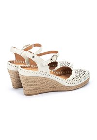 Sandalias de cuña blancas con diseño perforado, correa ajustable para el tobillo y tacones envueltos en yute. Parte superior de cuero suave con forro interior en color marrón.