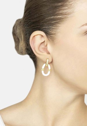 Close-up of a woman’s ear wearing a gold and white oval-shaped hoop earring with embedded small crystals.