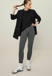 Sive uske tajice u rebrastom uzorku uparenih s crnim oversized sakoom i majicom. Nosene s bijelim Adidas tenisicama i bijelim čarapama.