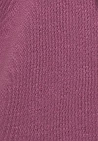 Tessuto lavorato a maglia di un morbido color rosa medio. La texture presenta una fine costina con cuciture uniformi e una leggera lucentezza.