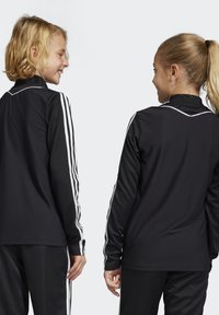 Zwarte sportjacks met lange mouwen, voorzien van witte verticale strepen aan de zijkanten en een gestructureerd stoffenpatroon.