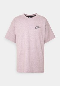 Světle růžové tričko vyrobené z měkké látky; uvolněný střih s krátkými rukávy. Obsahuje malé, vícebarevné logo Nike na hrudi.