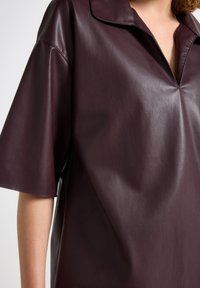 Burgundy faux læder skjorte med kort krave, afslappet pasform og korte ærmer. Glat tekstur og minimal detaljering.