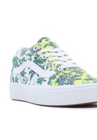 Baskets basses avec semelle blanche et motif floral en vert, bleu et jaune, avec lacets blancs et bande emblématique sur le côté.