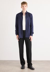 Navy button-up shirt with long sleeves, paired with black trousers and black shoes. Clean lines and a tailored fit create a modern look.