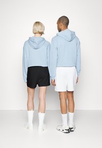 Aksessories bestående av blå hettegensere i et kort design, kombinert med svart-og-hvitt-shorts. Fotwear inkluderer hvite kne-høye støvler og sporty sko, satt mot en enkel bakgrunn.