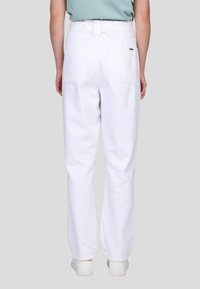 Pantalon en coton blanc avec une coupe décontractée, poches arrière et passants de ceinture. Texture lisse avec une finition soignée, associé à des baskets blanches.