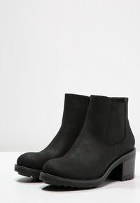 Botas negras hasta el tobillo fabricadas en suave ante, con paneles laterales elásticos, un tacón grueso y suela texturada antideslizante, presentando un diseño liso y limpio.