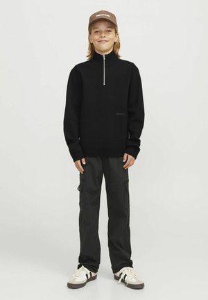 Schwarzer Zip-Kragen-Pullover mit langen Ärmeln, kombiniert mit dunklen Cargo-Hosen. Als Accessoires wird eine braune Kappe getragen. Freizeitbekleidung in Weiß mit schwarzen Streifen.