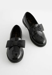 Chaussures en cuir verni noir avec une finition brillante, ornées d'un grand nœud en ruban noir à l'avant et d'une semelle basse et durable.