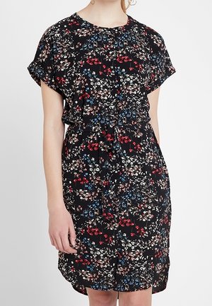 Woman wearing a black knee-length dress with red, white, and blue floral print, short sleeves, and a tied waist belt.