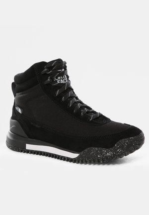 Bota de senderismo negra que presenta una combinación de tela sintética lisa y ante, suela texturizada con motas y cordones negros.