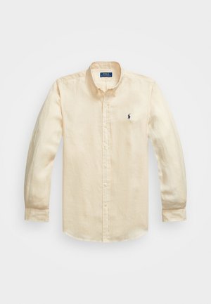 Camisa abotonada de manga larga en algodón color beige claro, con un cuello clásico y un pequeño logo en navy en el lado izquierdo del pecho.