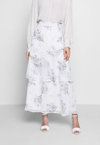 Weißer, fließender Maxirock mit gestuften Lagen und floralem Muster in Lila und Grün. Durchsichtige Textur mit dezenten Verzierungen überall.