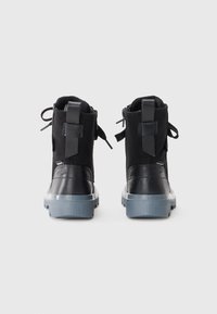 Botas negras hasta el tobillo con parte superior de ante y acentos de cuero brillante. Presentan una gruesa suela de goma gris y lengüetas para facilitar el uso.