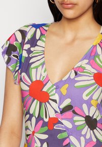 Vestido floral com uma base roxa e desenhos coloridos de margaridas e corações, decote em V e mangas curtas com babados. Dois botões na parte da frente.