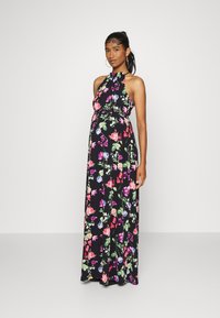 Vestido maxi com decote halter, fundo preto e padrões florais brilhantes em rosa, roxo e verde. Tecido fluido, corpete justo.