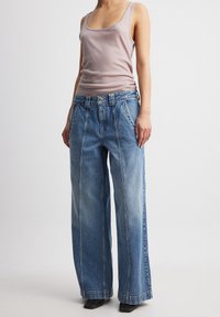 Svetlo vijolična majica bez rukava uparena s visokim strukom širokim svijetloplavim trapericama koje imaju šivane šavove i suptilnu teksturu blagog izblijedjenja.