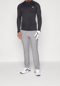 Mustat pitkähihaiset urheilupaidat, joissa on valkoinen logo, yhdistettynä vaaleanharmaisiin housuihin ja valkoisiin lenkkareihin, joissa on tummansinisiä raitoja. Golfkätensä on vasemmassa kädessä.