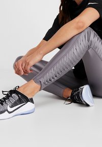 Leggings atléticos grises con un diseño ajustado, que presentan un panel texturizado a lo largo de los lados. Unas zapatillas en blanco y negro completan el atuendo.