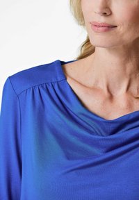 Blaues drapiertes Oberteil aus weichem, leichtem Stoff mit einem Schalkragen und Faltendetails an den Schultern.