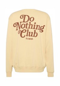 Sudadera amarilla con el texto "Do Nothing Club" en grandes letras cursivas marrones en la parte posterior, con puños y dobladillo acanalados.