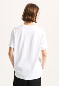 White cotton t-shirt with a classic crew neck, short sleeves, and a relaxed fit. Smooth texture and no visible patterns or graphics.