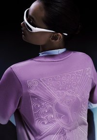 Paarse sweatshirt met reliëfontwerp op de rug, met draaiende patronen en een centraal embleem, gecombineerd met witte zonnebril.