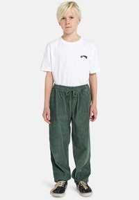 Groene corduroy broek met een elastische tailleband en een trekkoord, gecombineerd met een wit T-shirt met een klein zwart logo.