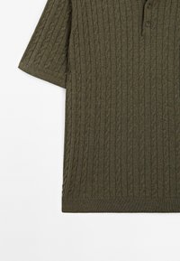 Polo a maniche corte, di colore verde oliva, realizzato in maglia con un motivo a treccia testurizzato, due bottoni al colletto e orli a coste su fondo e maniche.