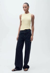 Žltý pruhovaný top na ramienka v kombinácii so širokými čiernymi džínami. Modelka má na sebe čierne sandále; vlasy má v úzkych vrkočoch. Jednoduchá, čistá estetiky.