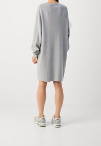 Robe-pull oversize grise à manches longues, col côtelé et coupe droite. Associée à des baskets gris clair.