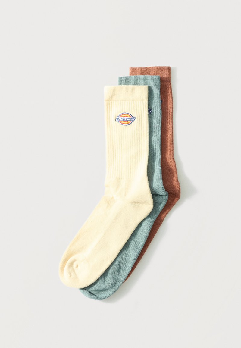 Τρία διπλωμένα αθλητικά καλτσάκια σε εκρού, απαλή τιρκουάζ και σκουροκόκκινη απόχρωση, με στρογγυλή ταμπέλα λογότυπου στη μανσέτα της εκρού κάλτσας.