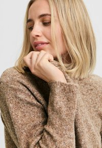 Brauner Strickpullover mit hohem Kragen, aus einem weichen, strukturierten Stoff und mit gerippten Bündchen. Das Design ist lässig und figurbetont.