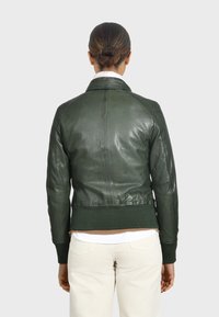 Giacca di pelle verde con una texture liscia, polsini e colletto a coste. Presenta un design aderente e dettagli di cucitura delicati sulla schiena.