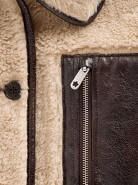 Jaqueta de couro castanho com forro de pele de ovelha. Apresenta um fecho de botão, bolso com zíper e costura distintiva ao longo das bordas.
