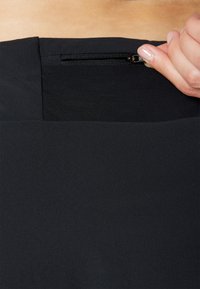 Tela negra con una cinturilla texturizada que incluye un bolsillo con cremallera oculta. Superficie suave con un diseño minimalista y sin patrones o adornos visibles.