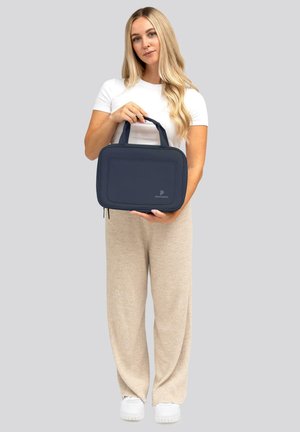 Borsa in tessuto blu navy, forma rettangolare, con manici superiori e una tasca frontale. Presenta una superficie liscia e un dettaglio del logo sulla parte anteriore.