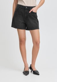 Shorts en denim noir à taille haute, avec poches avant et coupe décontractée. Le tissu a une texture lisse et un léger brillant.