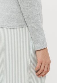 Un haut à manches longues gris côtelé associé à une jupe rayée vert clair et blanche. La manche a un poignet ajusté, et la jupe a une couture latérale.
