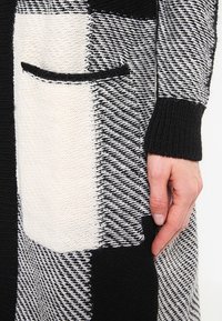 Cardigan a righe bianco e nero con lavorazione a maglia testurizzata, grande tasca frontale e polsini a costine, caratterizzato da un mix di trame fitte e aperte.